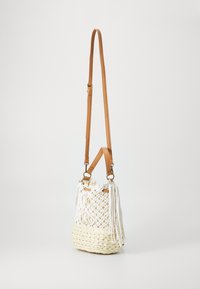 Sac tissé avec un motif en crochet blanc et une base tressée beige. Dispose de sangles en cuir marron et de pompons décoratifs sur le côté.