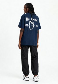 T-shirt marine avec un graphique blanc "Mi Amor" et des flèches au dos. Associé à un pantalon cargo noir et des baskets blanches. Conception décontractée.