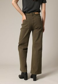 Pantalons larges couleur kaki en coton, avec une taille haute, des poches arrière et une étiquette en cuir marron sur la ceinture.