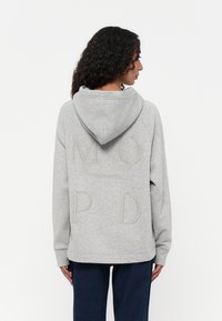 Grijze hoodie met een grote capuchon, raglanmouwen en getextureerde geborduurde letters "M O P D" op de achterkant. Zachte katoenmix.