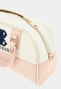 Canvas-Handtasche mit einem cremefarbenen Körper, rosa Lederakzenten und goldenen Beschlägen. Besitzt einen Reißverschluss und gestickte Logodetails.