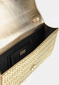 Auksinės metalinės rankinės su audiniu tekstūruotu paviršiumi. Yra juodas vidus, magnetinė uždanga ir mažas logotipo ženkliukas.