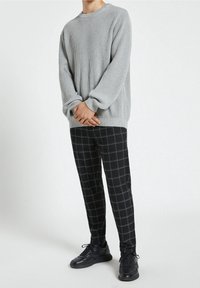 Szary sweter prążkowany z długimi rękawami, w połączeniu z czarnymi spodniami w kratę. Model w czarnych sneakersach. Prosty, prosty fason.