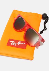 Červené plastové slnečné okuliare s gradientovými sklami položené na oranžovej mäkkej puzdre, ktorá má červenú nálepku s bielym logom "Ray-Ban".
