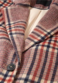 Chaqueta de lana a cuadros en tonos rojos, azules y crema. Presenta un cuello con muescas, un solo botón y una tela suave al tacto.