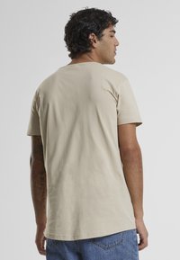 Beige pamut póló kerek nyakkal, rövid ujjú, laza szabású, kék farmernadrággal párosítva. Sima textúra.