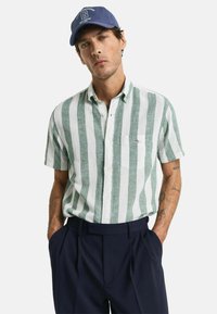 Camisa de manga corta con botones, en tejido con rayas verticales verdes y blancas, hecha de un material texturizado, que cuenta con un bolsillo en el pecho y un corte casual.