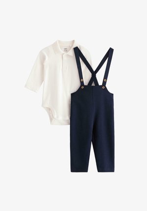 Bodysuit blanc à manches longues avec col polo à côté de salopette bleu marine avec bretelles réglables et accents en boutons en bois.