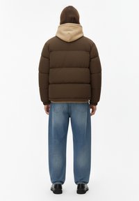 Giacca imbottita marrone con cappuccio beige, caratterizzata da un design trapuntato. Abbinala a jeans denim blu larghi e scarpe nere.