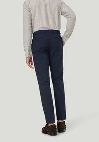 Marineblaue, taillierte Hose mit schmaler Passform, aus glattem Stoff, mit zwei Gesäßtaschen und kombiniert mit braunen Wildlederschuhen.