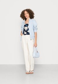Casaco bomber azul claro, blusa azul-marinho de flores, calças largas off-white e mala azul clara. Modelo usa sandálias achatadas.