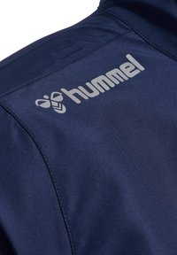 Mørkeblå polyesterjakke med en glat tekstur og det karakteristiske grå "hummel" logo på skulderen.