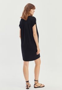 Czarna sukienka z krótkim rękawem o luźnym kroju i okrągłym dekoltem. Wykonana z miękkiego materiału i o minimalistycznym designie. Noszona z czarnymi sandałami na cienkich paskach.