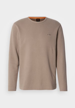 Camisa de manga larga color beige hecha de tela de canalé. Cuenta con un escote redondo y un pequeño logotipo bordado en el lado izquierdo del pecho. Acentuada con color naranja en el interior del collar.