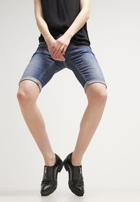 Denimové bermudy v středně modré barvě s ohrnutými lemy. Spárované s černými kotníkovými botami na zip. Jednoduchý design, standardní střih, casual styl.