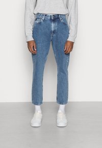 Jeans in denim blu chiaro con una vestibilità rilassata, vita alta e gambe dritte. Presentano cinque tasche e una leggera scoloritura. Indossati con sneaker bianche.