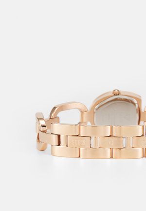 Roze gouden horloge met een metalen schakelband. Kenmerkt zich door gepolijste schakels en gegraveerde branding. Ronde kast met een subtiele textuur aan de achterkant.