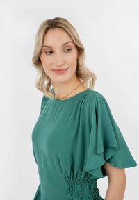 Abito verde con maniche corte a volant e dettagli arricciati in vita. Tessuto morbido e design fluido, con una vestibilità comoda.