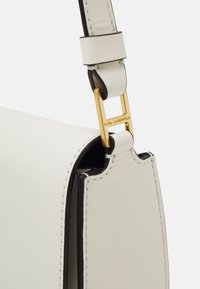 Sac en cuir blanc au design structuré, avec un fermoir en métal doré et des accents noirs. Couture détaillée le long des bords.