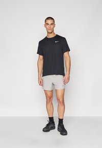 Crna Nike majica, svijetlosivi atletski šortsevi s plavim naglaskom i crne tenisice. Glatka tkanina, ležeran dizajn i atletski kroj.