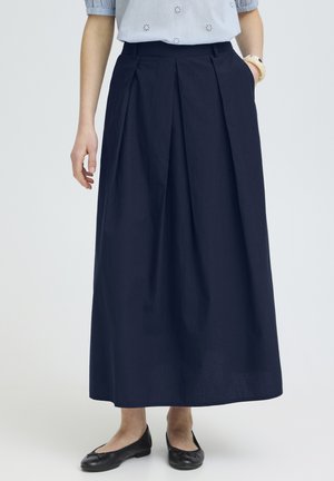 Ženska oblečena v mornarsko modro krilo dolžine do gležnjev z naborki, obuto v črne balerinke in oblečena v svetlo modro kratko-srajčno Bluzo.