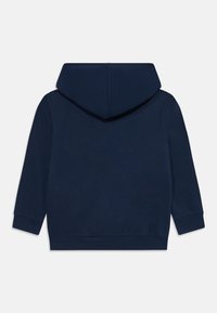 Mornarji modra kapuca s veliko, prostorno kapuco. Ima dolge rokave in rebraste manšete. Gladka tekstura, minimalistična zasnova, brez vidnih logotipov.