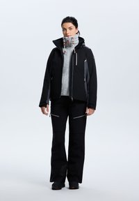 Giacca impermeabile nera con accenti grigi, colletto alto, cappuccio regolabile e tasche con zip. Abbinata a pantaloni neri con dettagli con zip.
