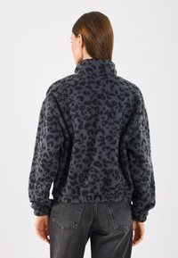 Pulover din fleece gri închis cu guler înalt, având un imprimeu texturat cu leopardi. Mâneci lungi cu o croială relaxată; se asortează cu blugi gri.