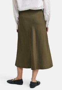 Olivenfarget midi-skjørt med et glatt, flytende stoff; har et enkelt design, høy midje og er parret med svarte vevde sko.