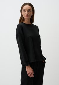 Felpa nera a maniche lunghe in tessuto morbido, caratterizzata da un collo a giro, vestibilità comoda e polsini a costine con un design minimalista.