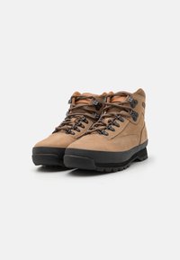 Scarpe da trekking marroni in pelle nubuck con suola in gomma. Presentano occhielli metallici, lacci marroni e colletto imbottito alla caviglia.