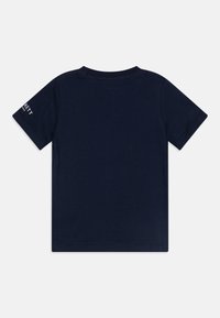 Tums zila kokvilnas T-krekls ar īsām piedurknēm, apaļu kaklu un vienkāršu aizmuguri. Uz piedurknes ir neliels balts logo teksts. Gluda tekstūra.
