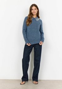 Blå stickad tröja med krage, med pärlornas detaljer vid kragen, i kombination med mörka jeanstygbyxor och sandaler med remmar.