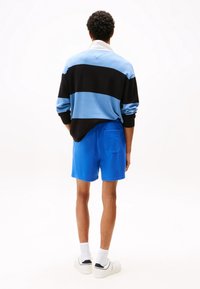 Světle modrý a černě pruhovaný svetr s bílým límečkem, spárovaný s modrými šortkami a bílými teniskami. Hladké textury a volný střih.