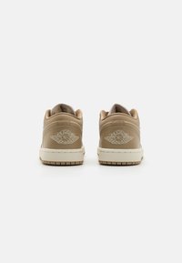 Baskets en cuir beige avec un col rembourré, dotées d'un logo Air Jordan brodé en blanc au niveau du talon et d'une semelle en caoutchouc texturé.