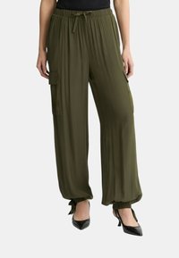 Pantalones de pierna ancha en verde oliva con cintura elástica y puños atados. Presenta bolsillos laterales tipo cargo y una textura fluida. Combina con tacones negros.