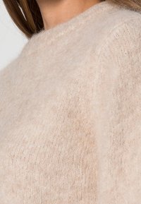 Maglione beige chiaro realizzato in un materiale morbido e peloso. Presenta un collo a giro e una vestibilità ampia con un motivo a maglia testurizzata.