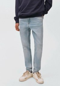 Vaqueros de mezclilla azul claro con un corte slim, que presentan un lavado desgastado, detalles de costura sutiles y se combinan con zapatillas crema.