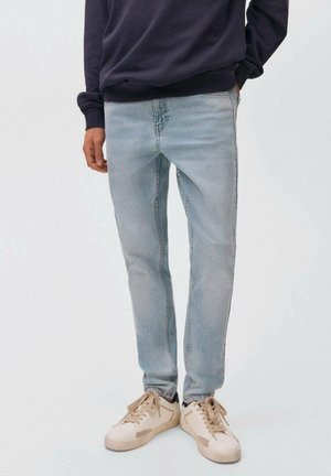 Vaqueros de mezclilla azul claro con un corte slim, que presentan un lavado desgastado, detalles de costura sutiles y se combinan con zapatillas crema.