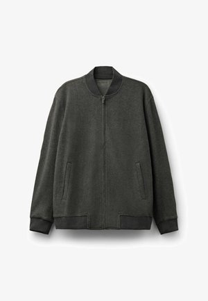 Tmavě zelená bomber bunda vyrobená z měkké tkaniny. Obsahuje zip na přední straně, boční kapsy, žebrované manžety a lem, a kulatý límec.