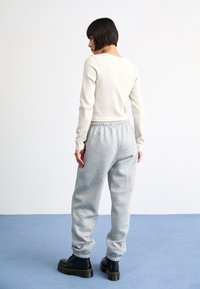 Helle graue Sweatpants mit elastischem Bund, kombiniert mit einem cremefarbenen, gerippten Langarmoberteil. Dazu schwarze klobige Stiefel. Glatte Stoffstruktur.