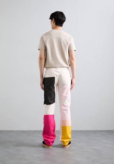T-shirt beige abbinato a pantaloni patchwork multicolori con pannelli neri, rosa e gialli. Tessuto liscio con una vestibilità comoda.