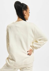 Lys beige oversized sweatshirt lavet af blødt stof, med en ribbet rund halsudskæring og afslappet pasform. Diskret tekstur og sænkede skuldre.