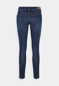 Jeans ajustados de denim azul oscuro con una textura suave. Dos bolsillos traseros con un patrón de costura sutil y una etiqueta de cuero con la marca en la cinturilla.
