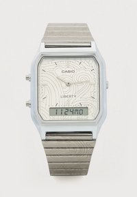 Cyfrowy zegarek Casio z srebrną bransoletą ze stali nierdzewnej. Posiada jasną tarczę z wzorami, prostokątną kopertę i cyfrowy wyświetlacz.