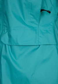 Tyrkysová bunda vyrobená z hladké, voděodolné tkaniny, s přední kapsou a nastavitelnou šňůrkou pro bezpečné nošení.