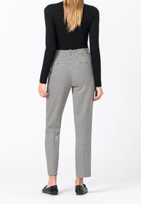 Pantaloni a scacchi houndstooth bianco e nero con vestibilità slim, vita alta, tasche laterali e gamba affusolata. Indossati con scarpe flat nere.