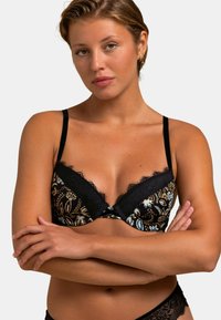 Bralette en dentelle noire avec un motif floral en bleu et or, cups triangulaires avec des bords festonnés et bretelles ajustables fines.