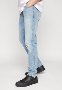 Vaqueros azul claro hechos de mezclilla, con un corte entallado, bolsillos estándar y detalles de costura, combinados con zapatillas negras.