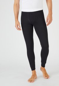 Leggings de algodón negro con un diseño ajustado, que presentan una cintura elástica y puños en los tobillos, exhibidos en un modelo descalzo.